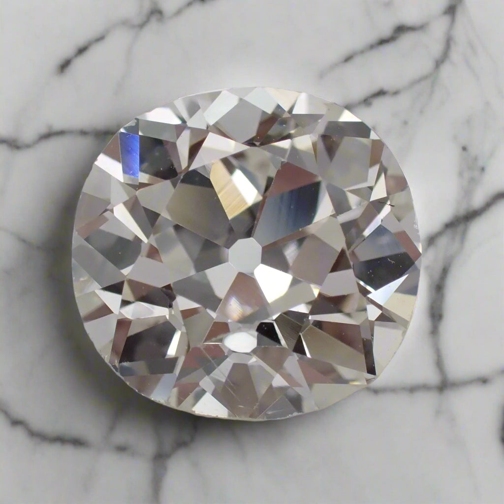An antique diamond, with uneven facets, rests on white marble. The diamond has a visible flat culet.