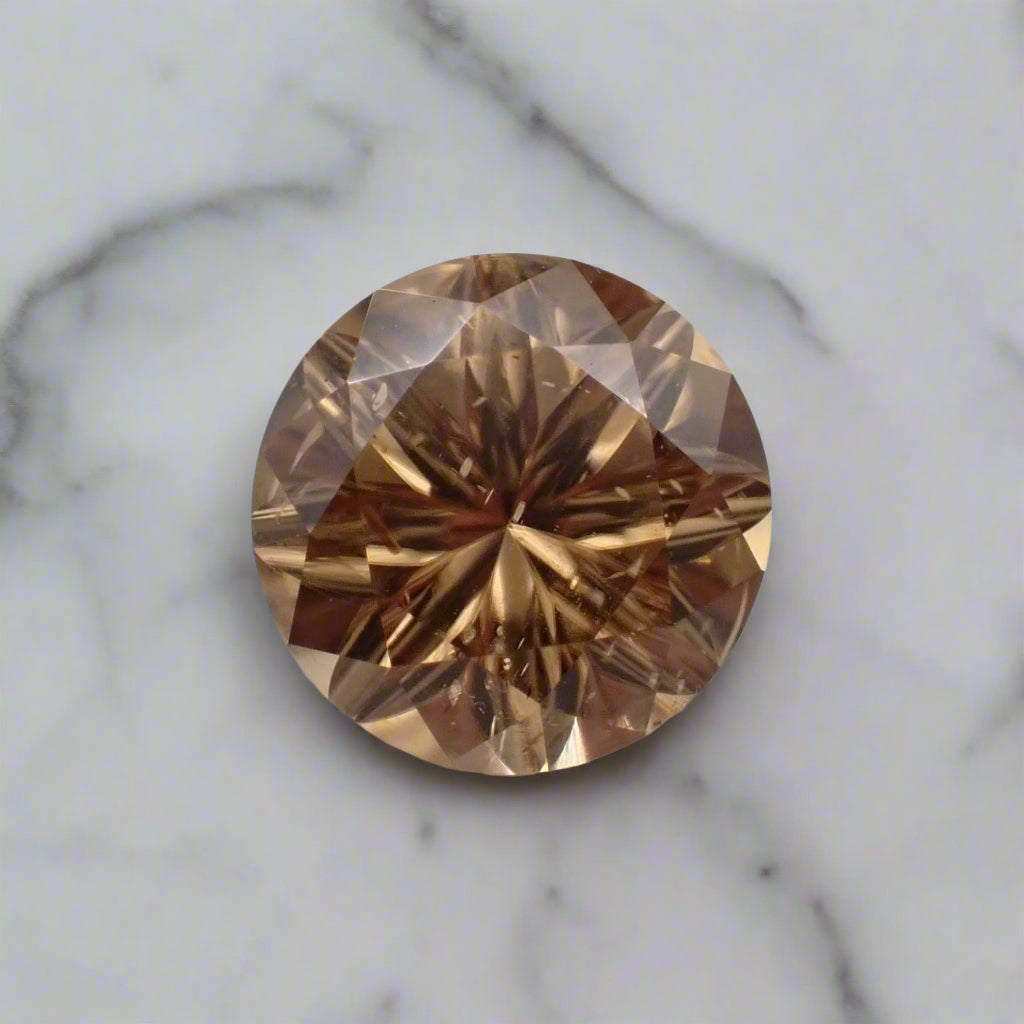 A bright champagne coloured zircon rests on a marble surface. The stone has small inclusions that are visible.