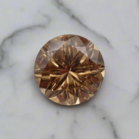 A bright champagne coloured zircon rests on a marble surface. The stone has small inclusions that are visible.