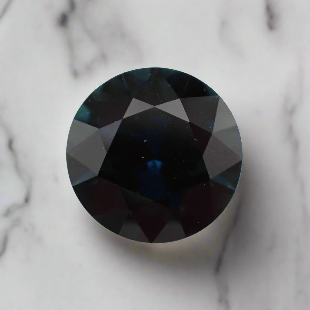 A round, dark blue sapphire, rests on a white marble surface.