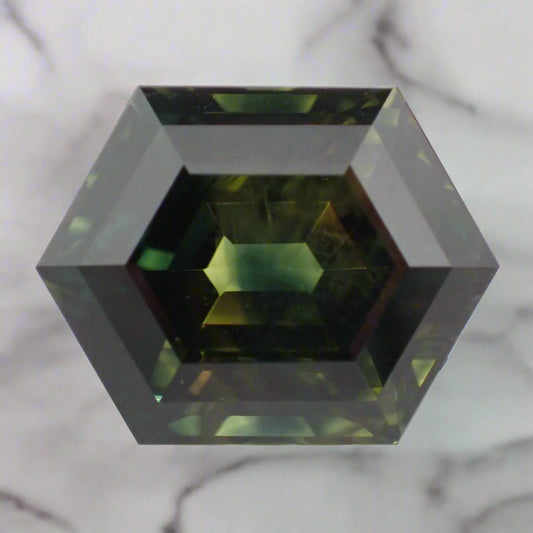 A rich green sapphire rests on a marble surface. The sapphire is a hexagonal step cut.