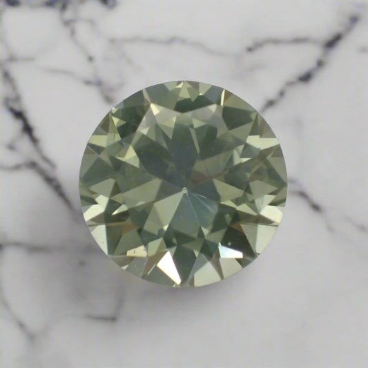 A pastel green, round sapphire rests on white marble.