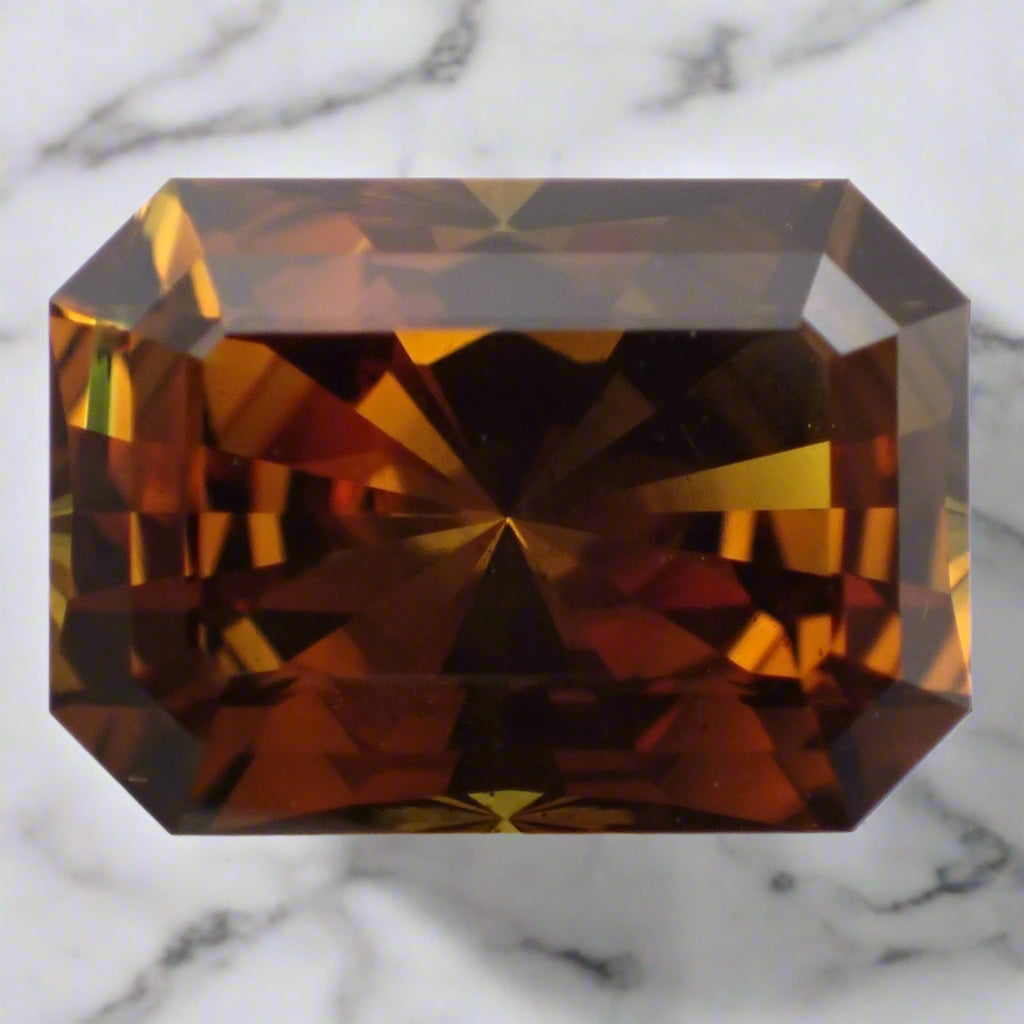 A vivid orange-brown sapphire rests on marble. The sapphire is rectangular with cropped corners.