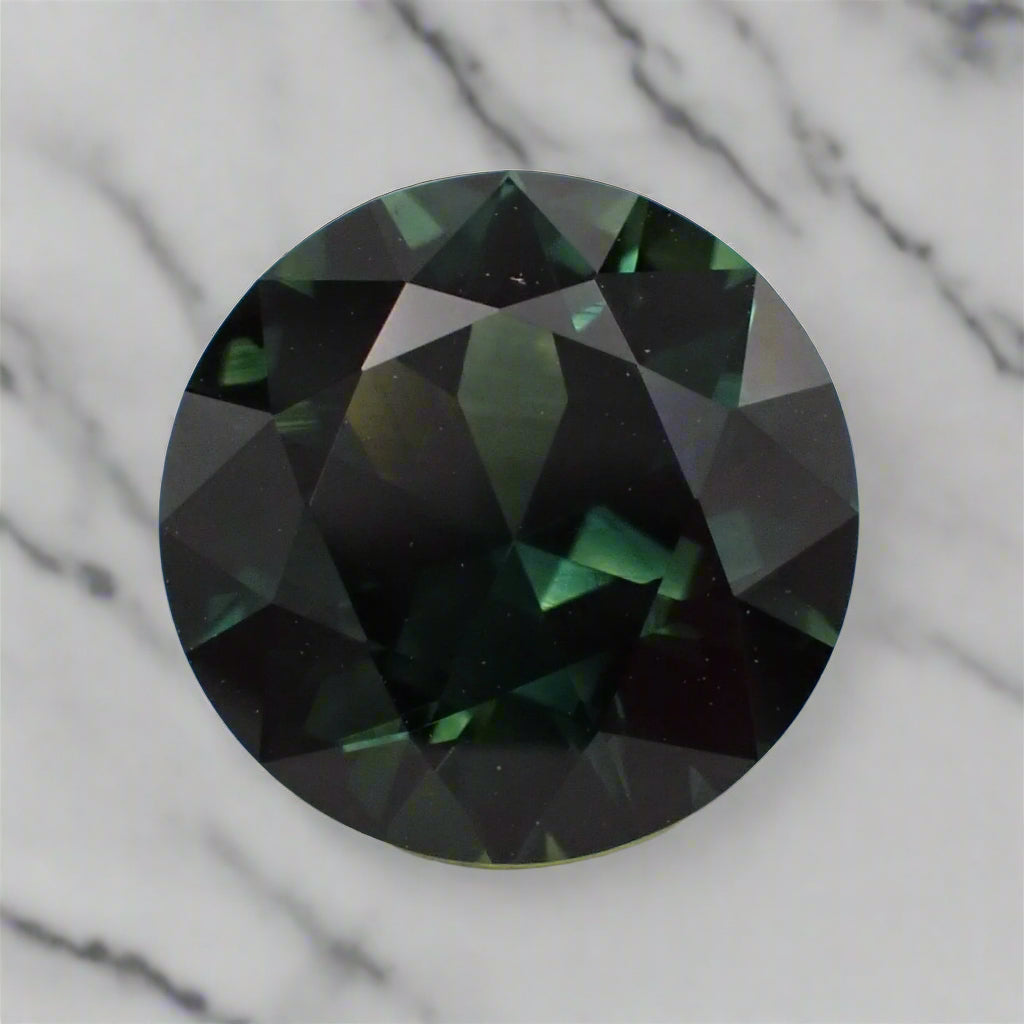A large, round, dark green sapphire rests on a marble surface.