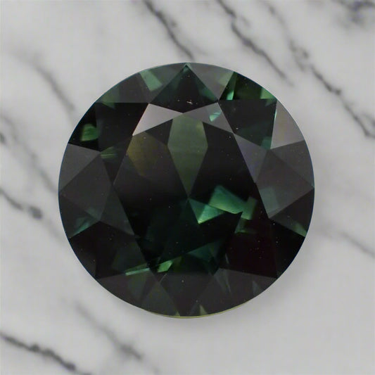 A large, round, dark green sapphire rests on a marble surface.