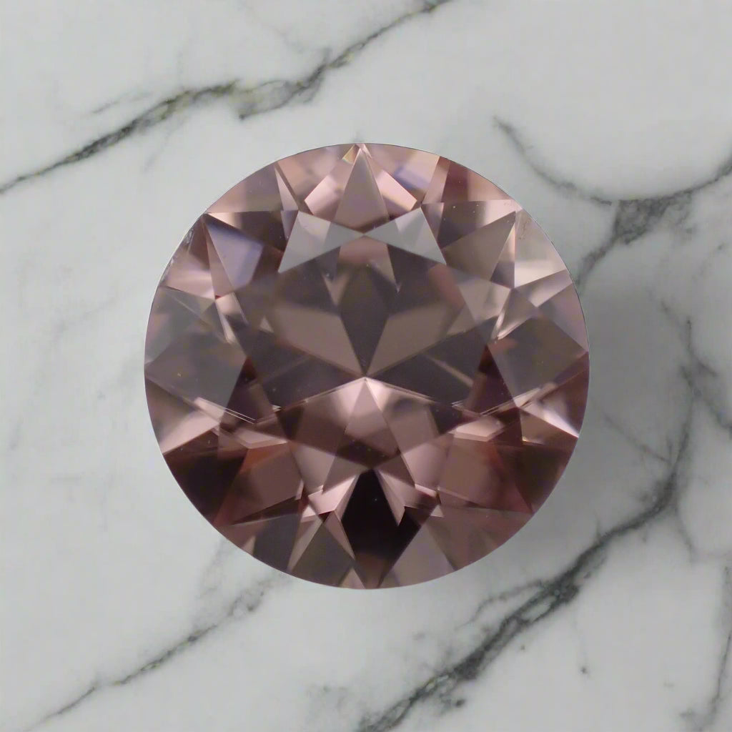 A dusty pink zircon rests on a marble surface. The gem is round, clear and bright.