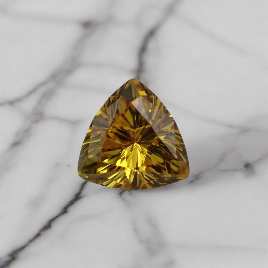 A rich yellow sapphire rests on marble. The stone is a soft triangle in shape.