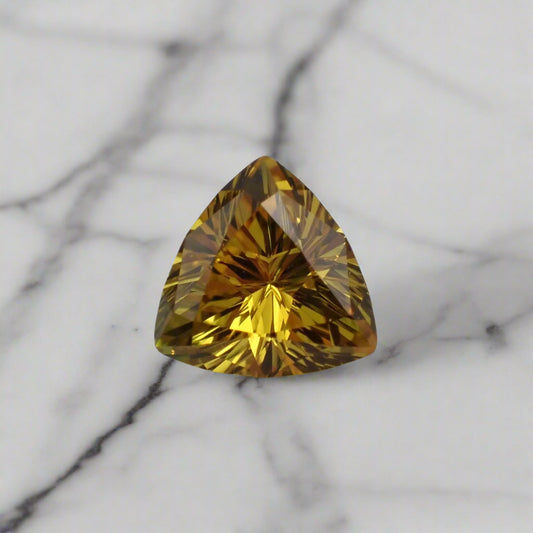 A rich yellow sapphire rests on marble. The stone is a soft triangle in shape.
