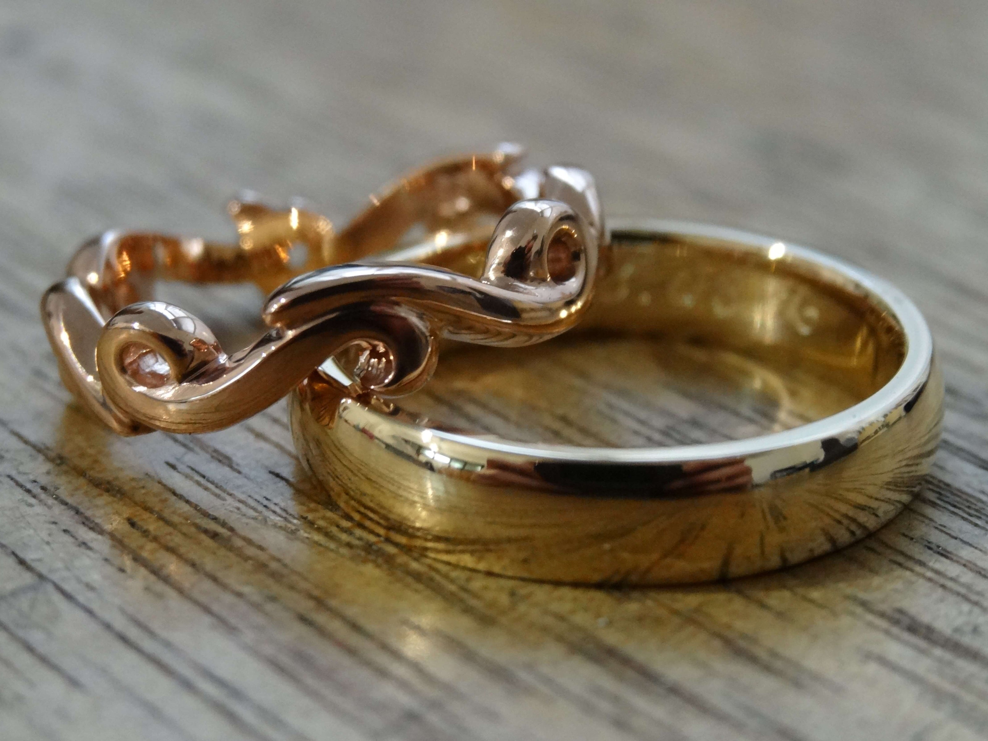 Rose gold continuous swirl wedding ring sitting on top of a yellow gold plain polished wedding ring on a wooden surface