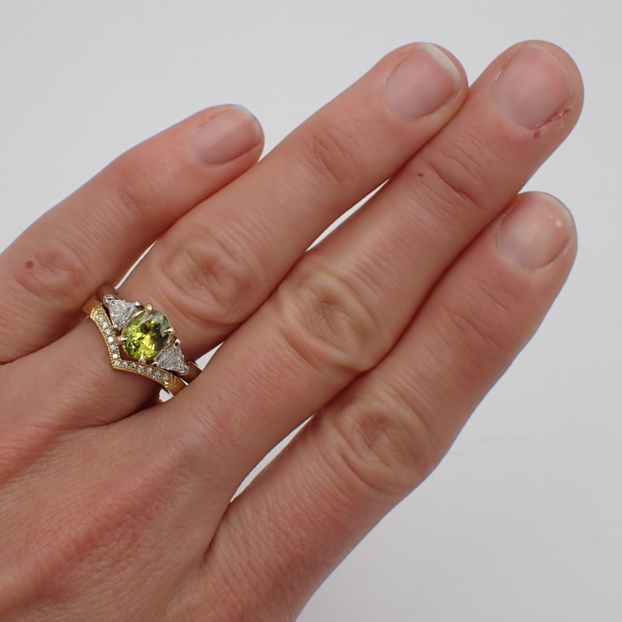An oval sapphire engagement ring with a pair of triangle diamonds is being worn on the ring finger with a fitted wedding ring.