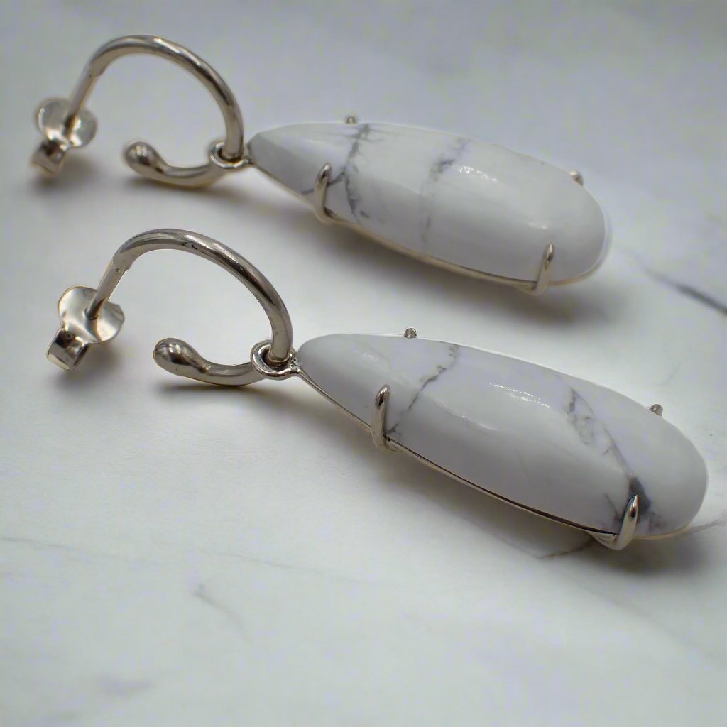 White, tear drop shaped, howlite charms hang from white gold loop earrings.