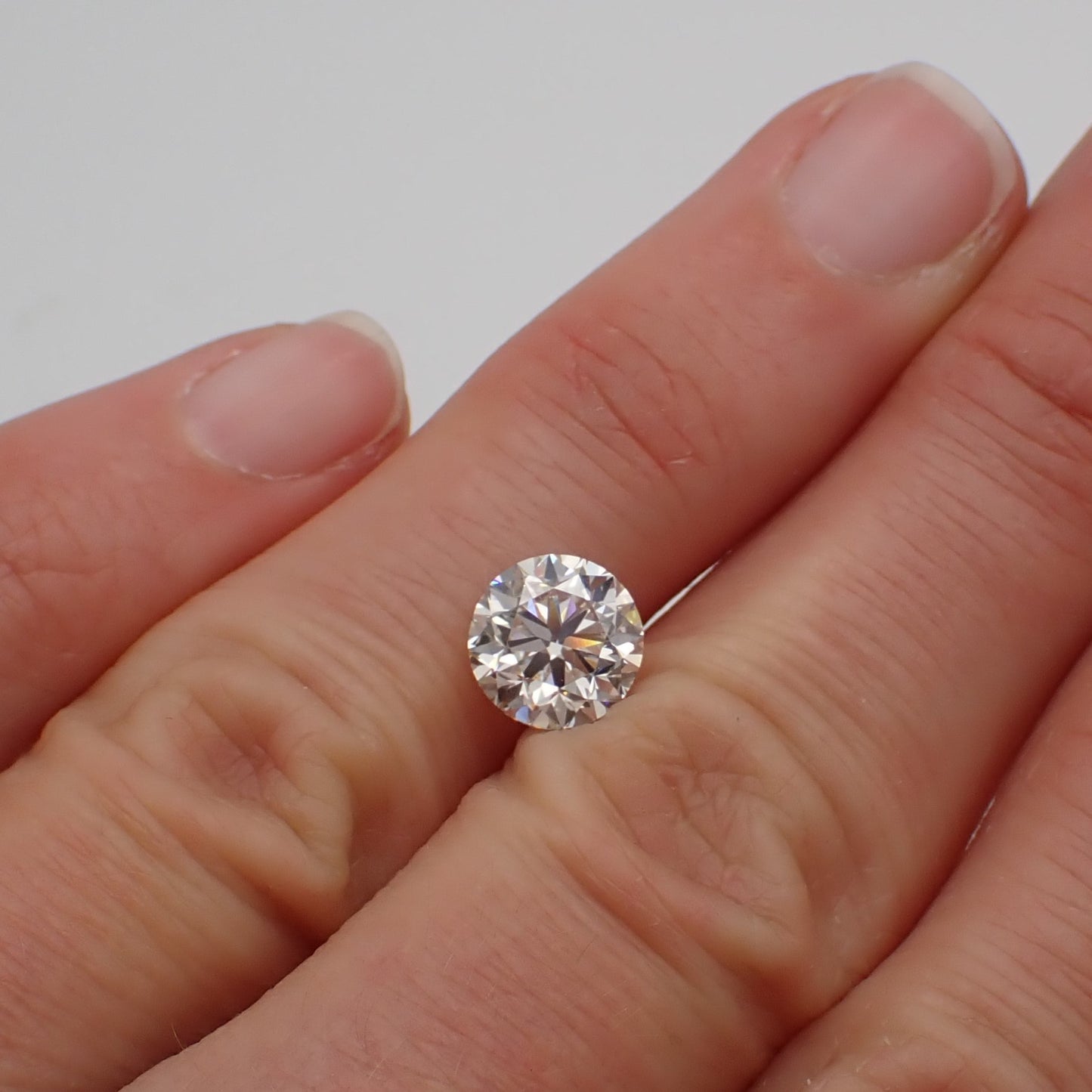 a 2 carat loose round white diamond rests between two fingers