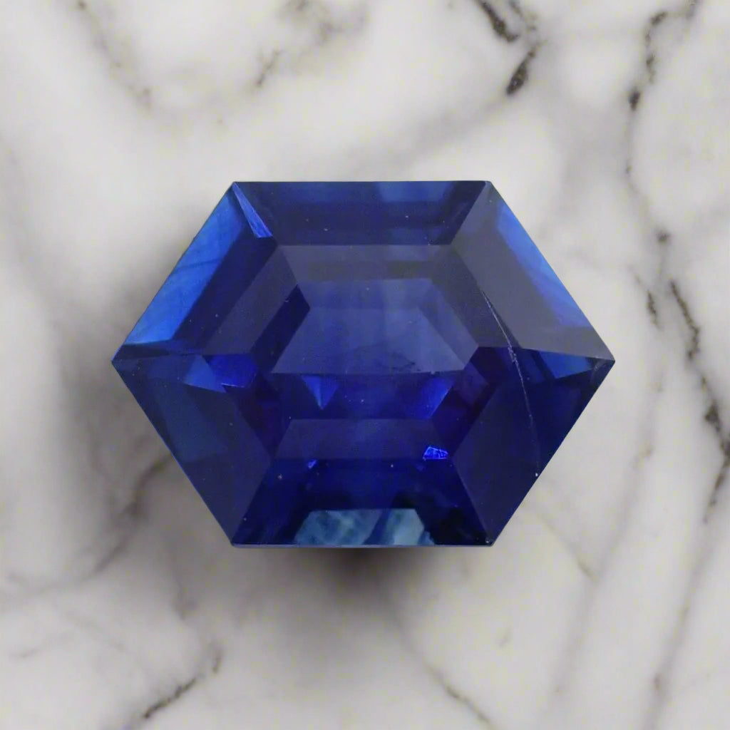 an intense, bright blue sapphire cut in an elongated hexagon rests on a white surface
