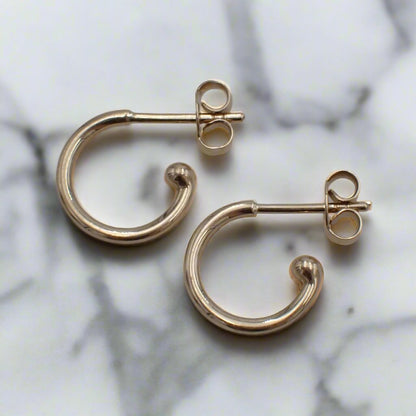 Yellow gold loop earrings with post and butterfly rest on a white surface.