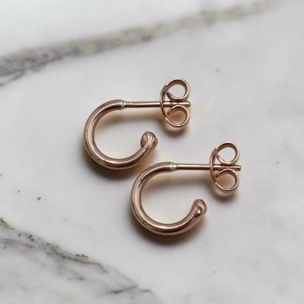 Small rose gold loop stud earrings rest on a white surface.