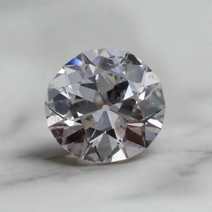 An Old European Cut diamond rests on a white surface with visibly uneven facets and small inclusions.