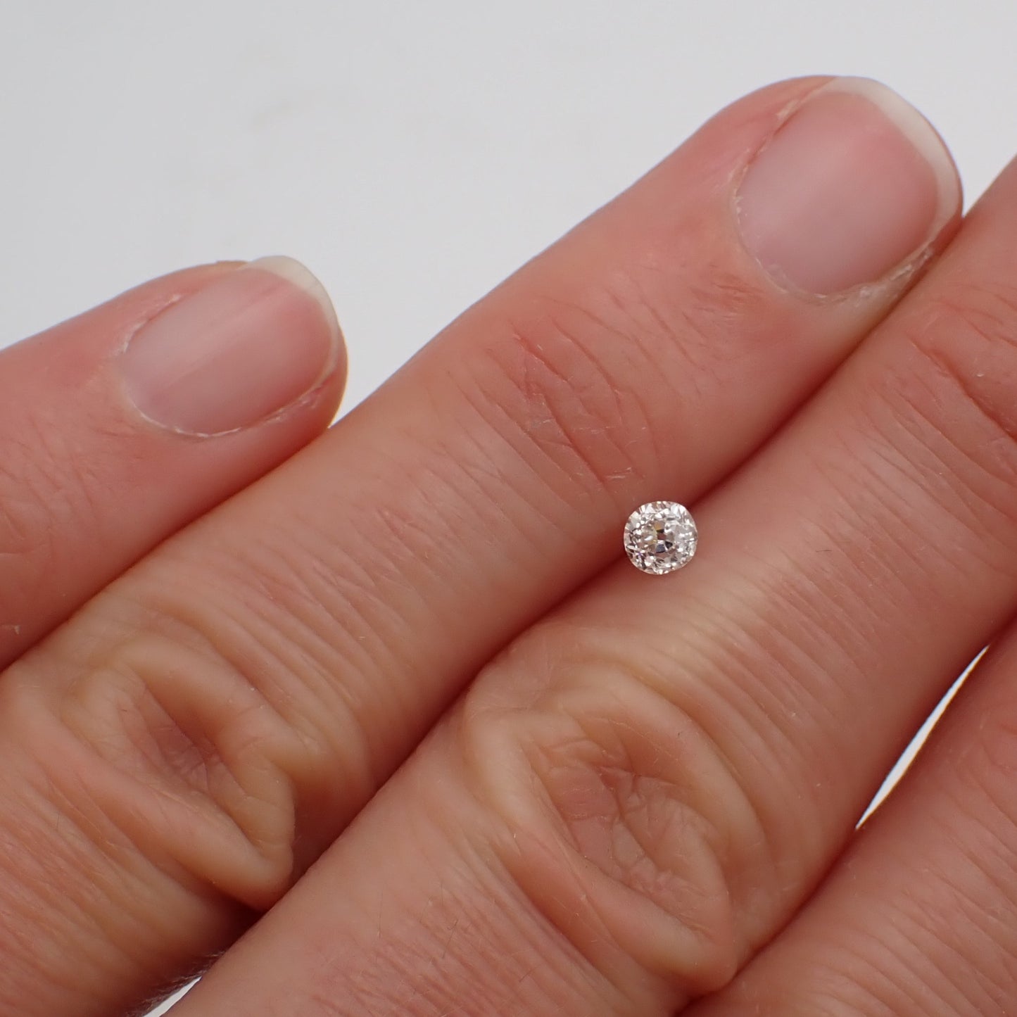 an antique diamond resting between two fingers to show scale