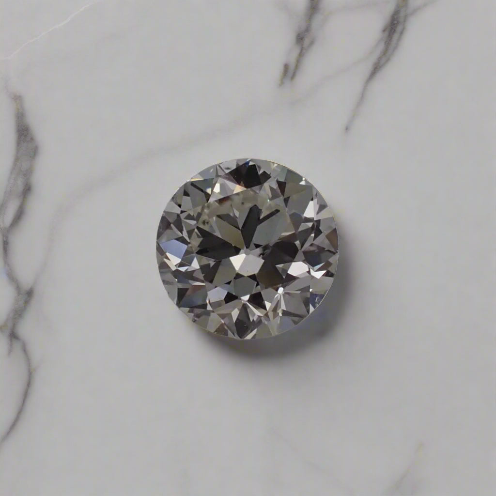 An antique diamond with slightly asymmetrical facets rests on a white marble surface