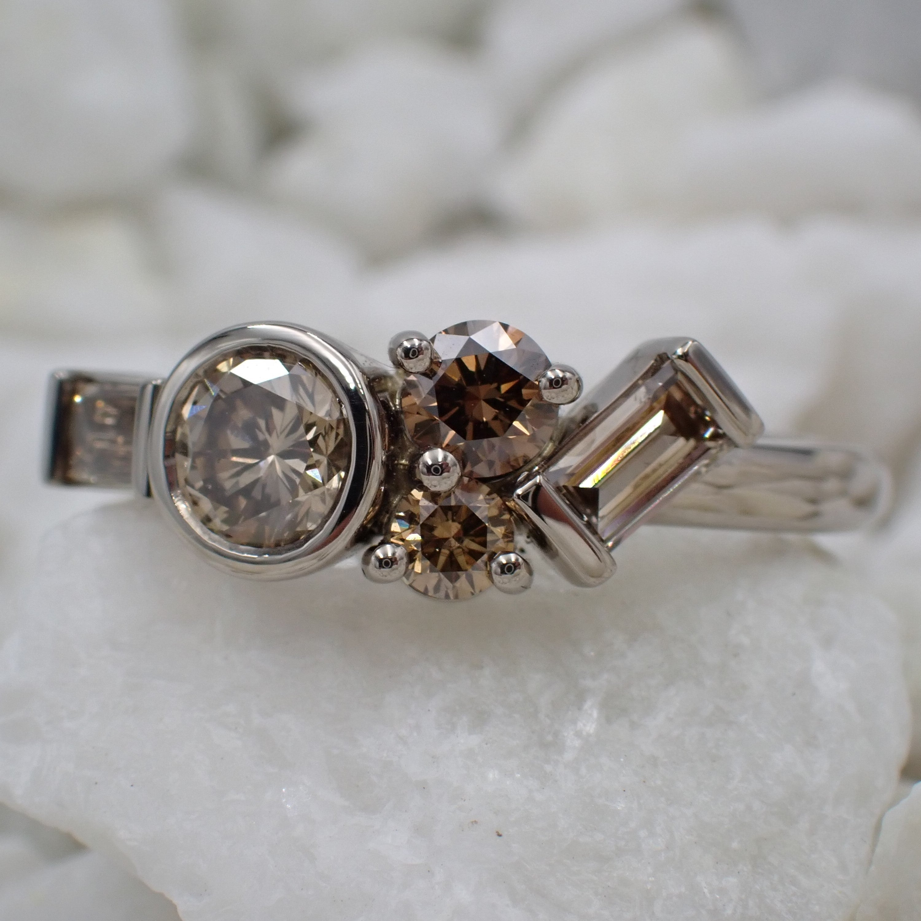 Five champagne diamonds set into a white gold ring. The diamonds are a mixture of browns and round and baguette cut.