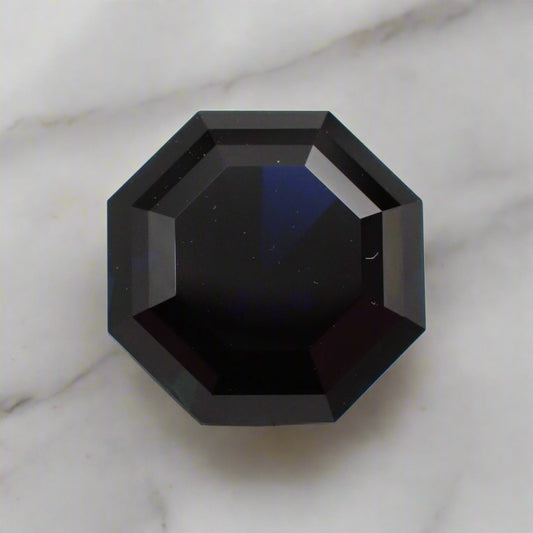 An octagonal sapphire, so dark blue it almost appears black, rests on a white marble surface.