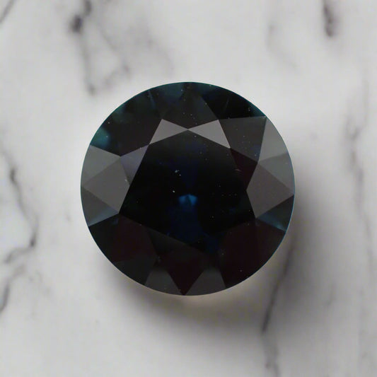 A round, dark blue sapphire, rests on a white marble surface. 