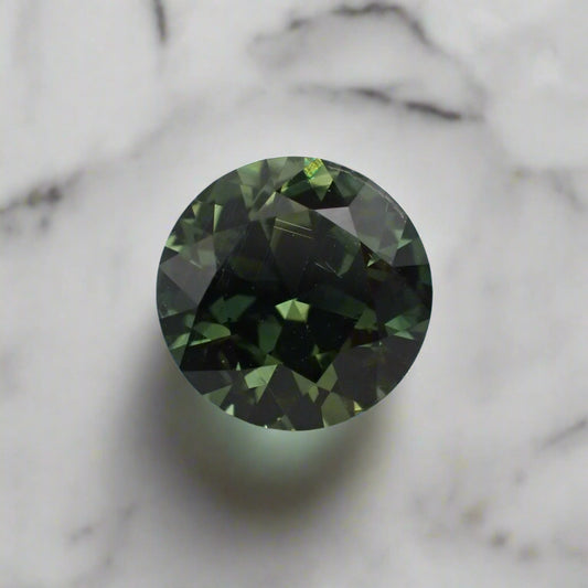 A round green sapphire, loose on a white marble surface. There are lots of bright green flashes visible.