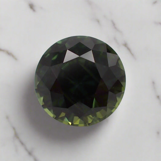 a dark green sapphire rests on a white marble surface. There are flashes of olive green and forest green visible.