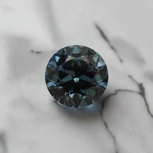 An Australian sapphire, in a pale blue, rests on a white marbled surface.