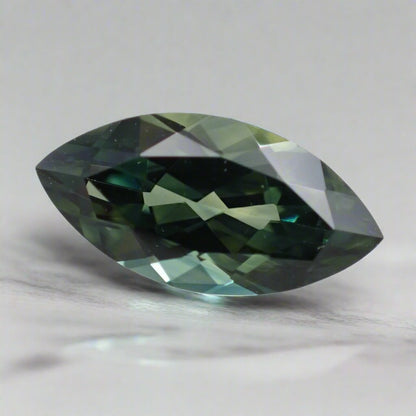 A marquise cut parti sapphire, displaying both green and blue, rests on a white surface.