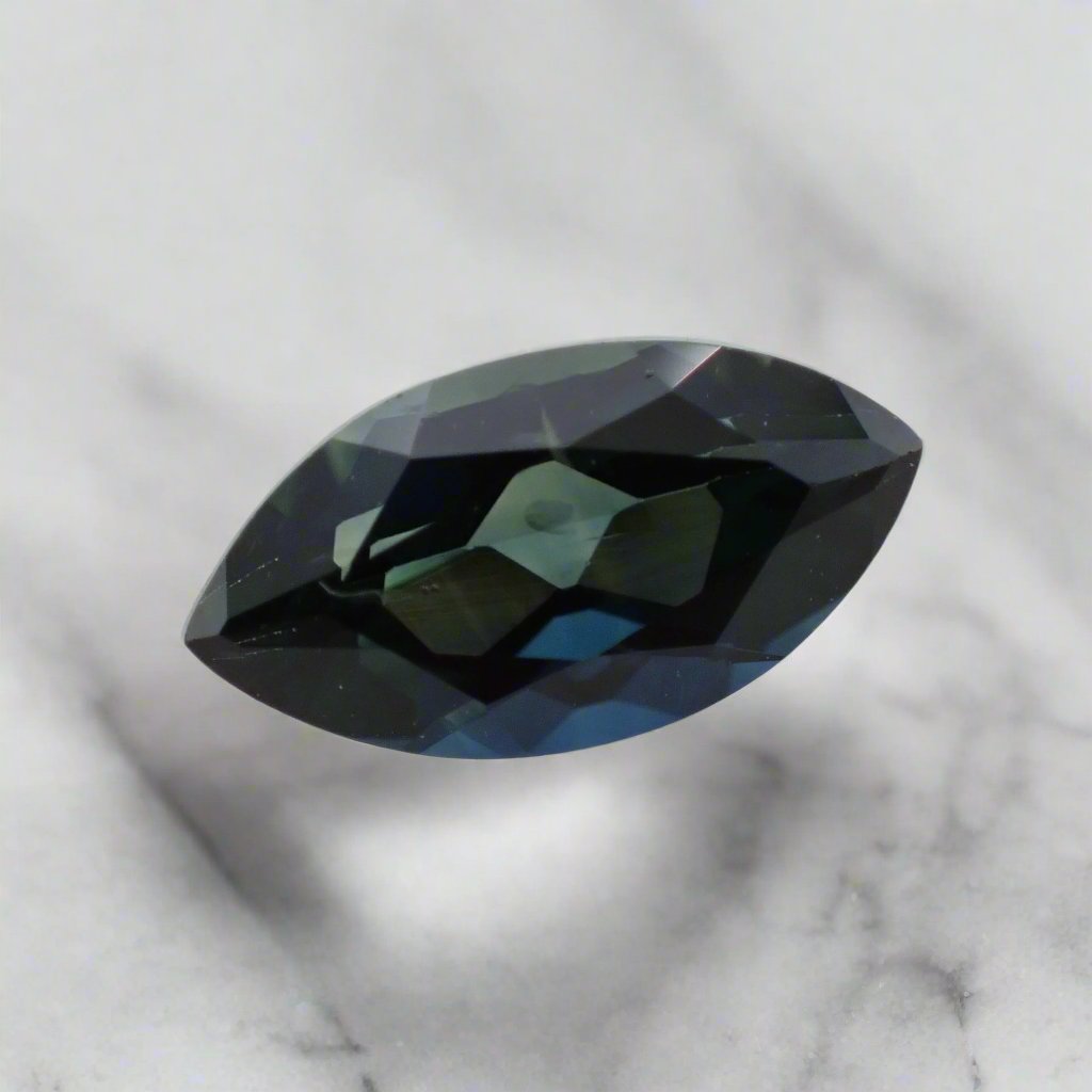 A parti sapphire, displaying both green and blue colouring, in a marquise shape rests on a white surface.