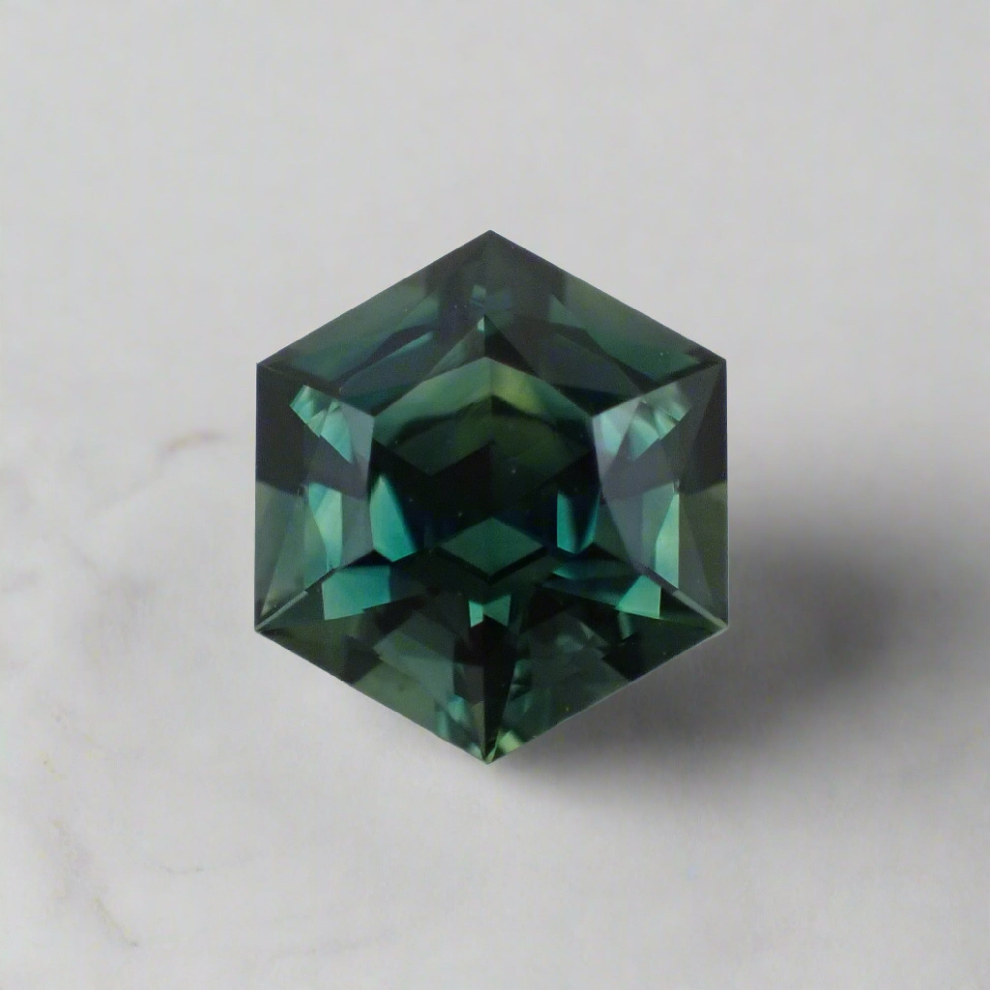 A teal sapphire cut into a hexagon shows flashes of teal, blue, green and yellow.