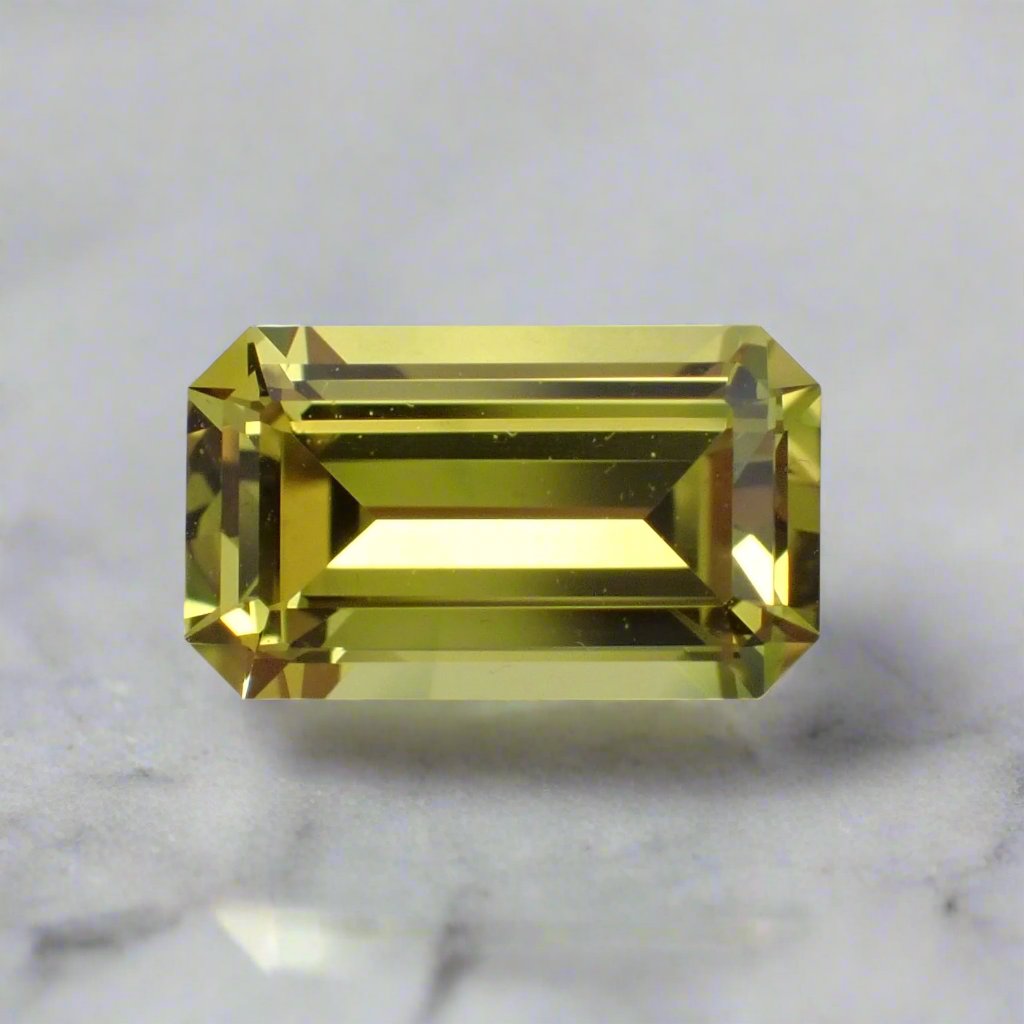 A vibrant, sunny yellow sapphire rests on a white surface. It is a rectangle shape with the corners cut off. 