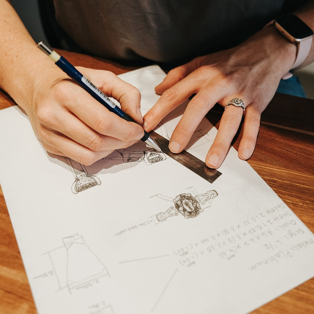 A three stone engagement ring is being drawn by hand by a jeweller.