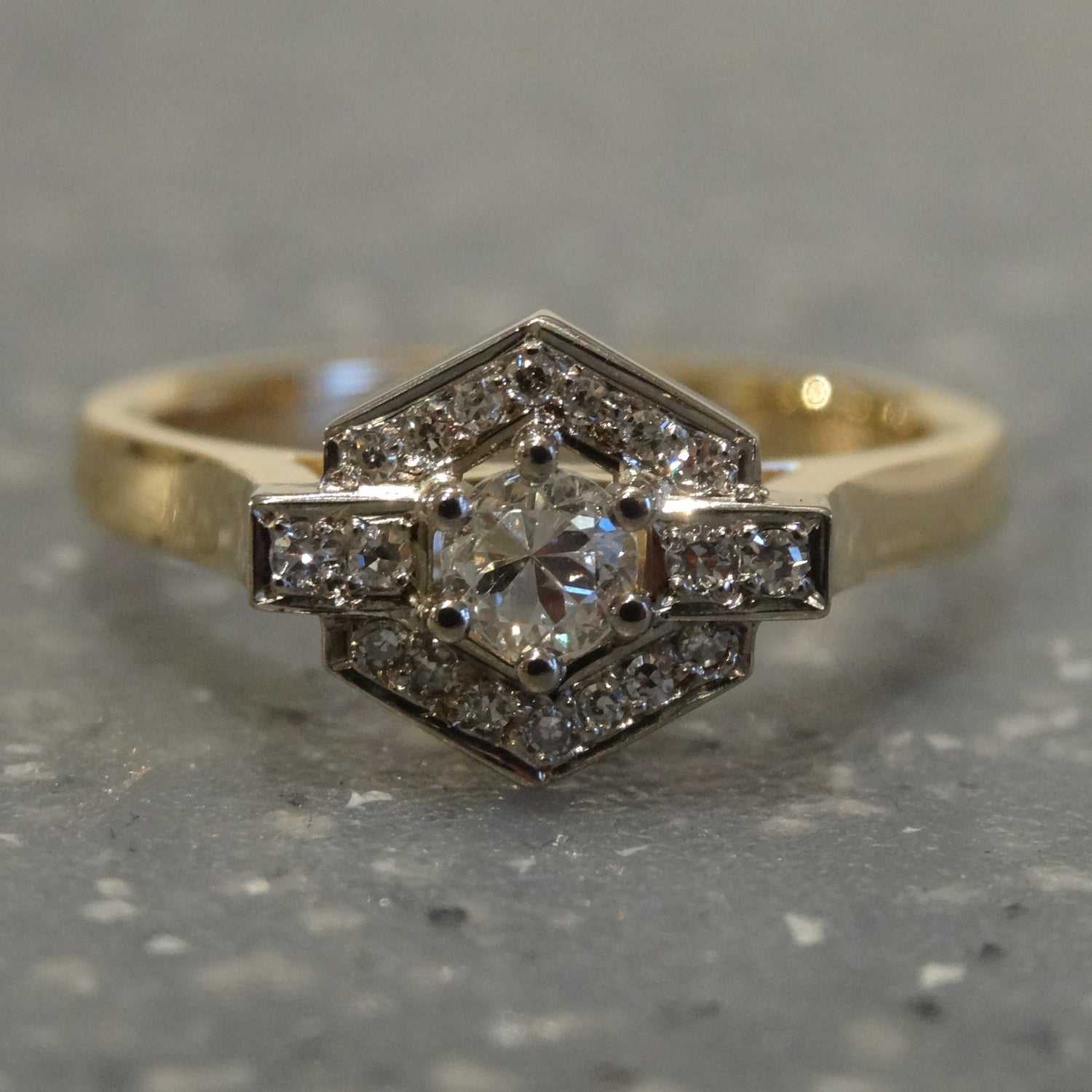 a two tone engagement ring set with one large round single cut diamond and a hexagonal halo set with small round diamonds