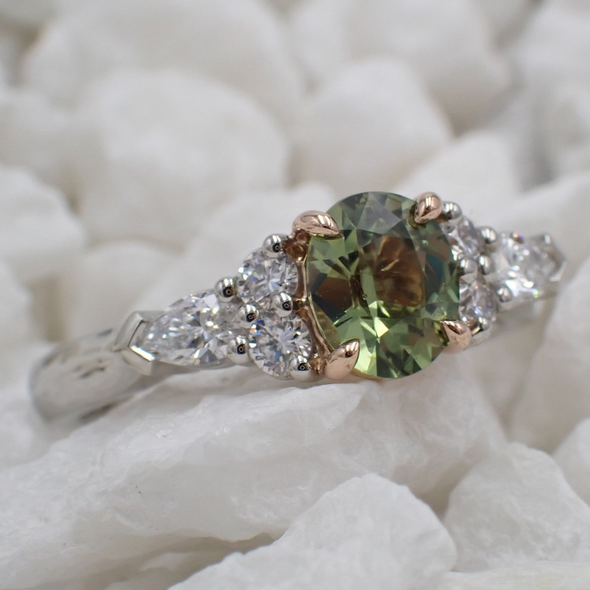 A pale green sapphire engagement ring with round and pear cut diamond shoulders.