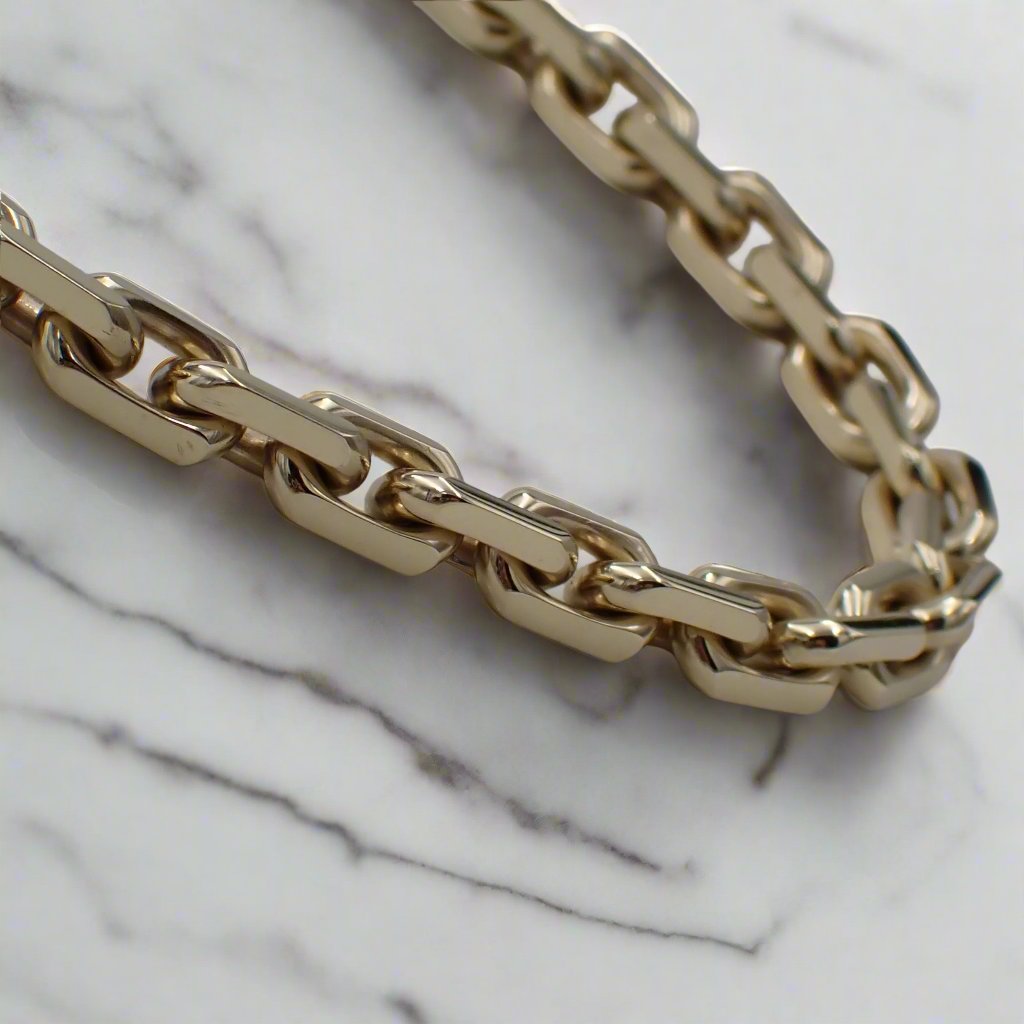 A solid gold, heavy link chain on white marble.