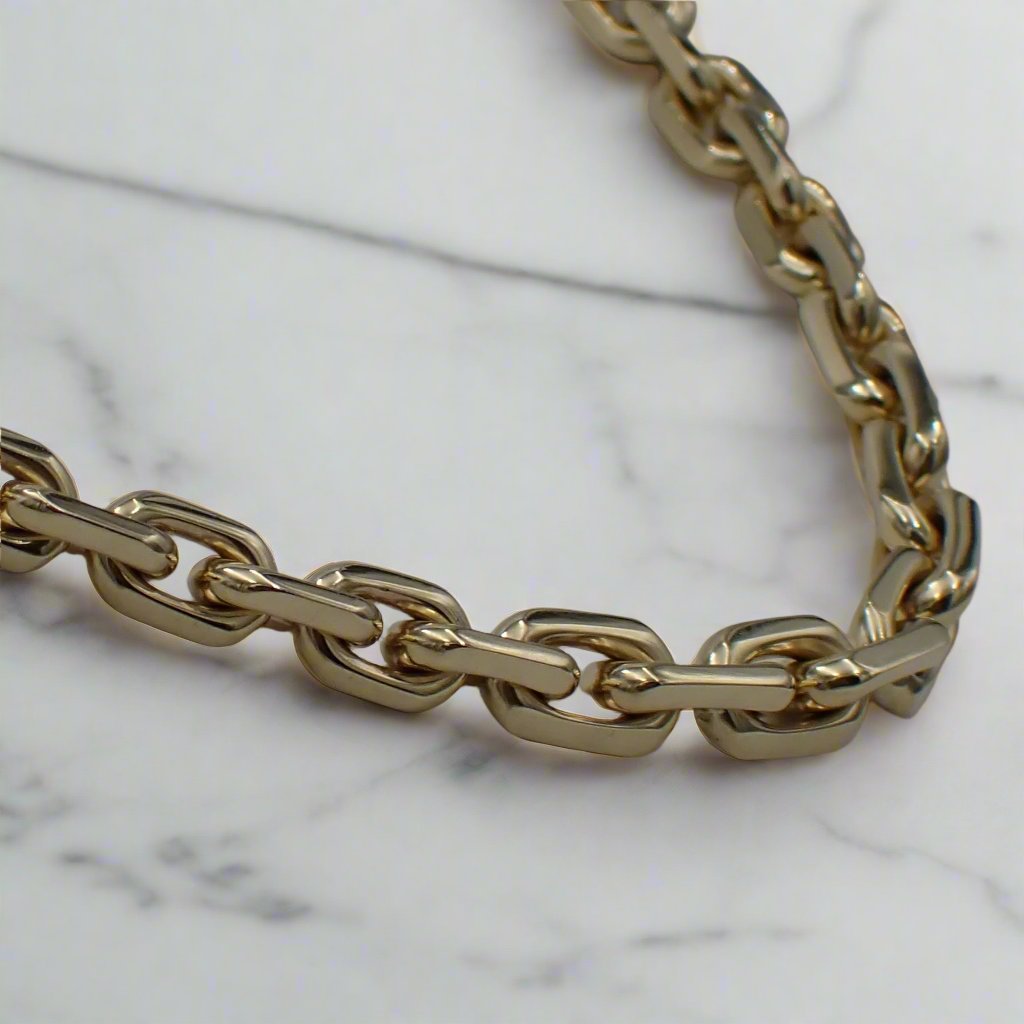 A segment of gold chain with graduating links is shown on a white surface.