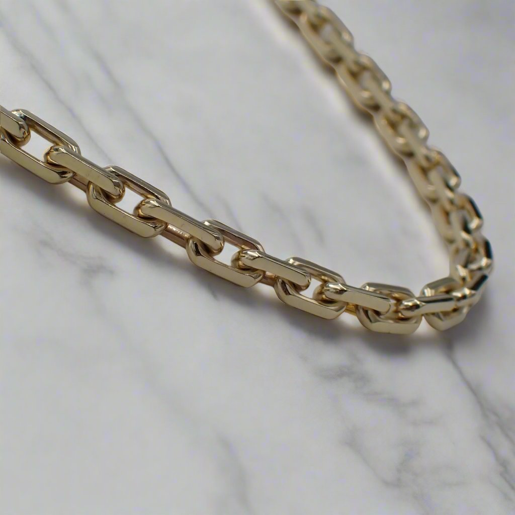 A solid gold chain with faceted links rests on a white surface.