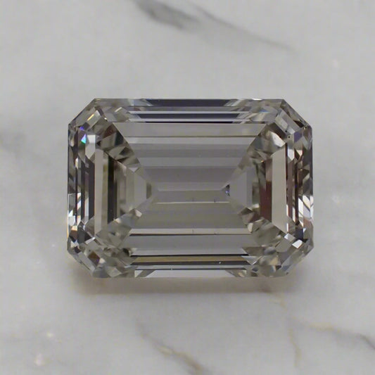 A rectangular emerald cut diamond sits loose on a white surface