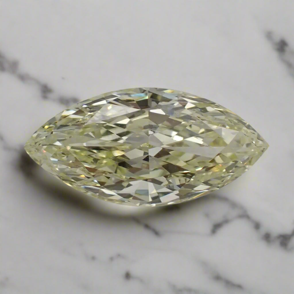 A light, bright yellow marquise cut diamond rests on a marble surface