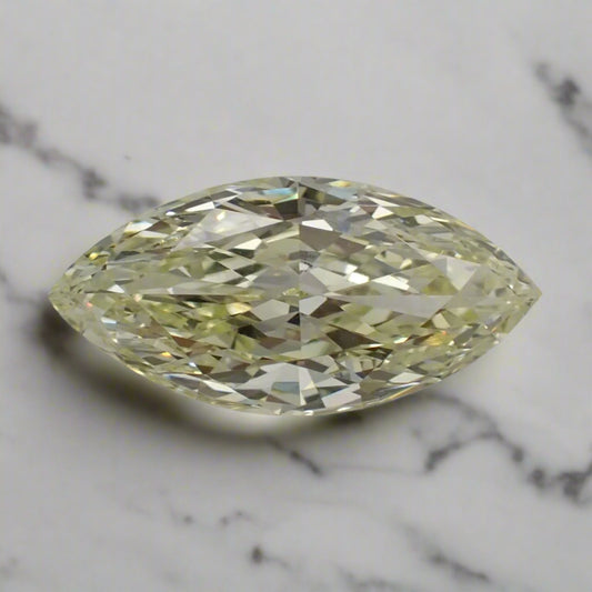 A light, bright yellow marquise cut diamond rests on a marble surface