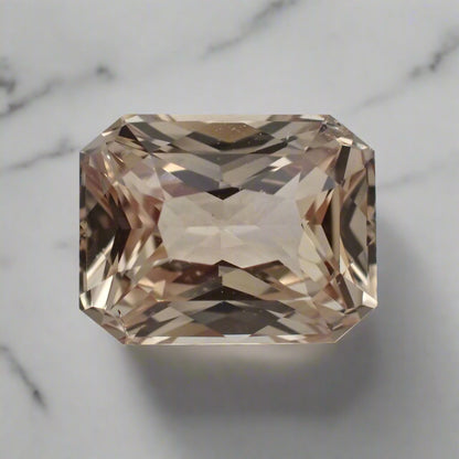 A bright peach sapphire rests on white marble. It is rectangular in shape, radiant cut.