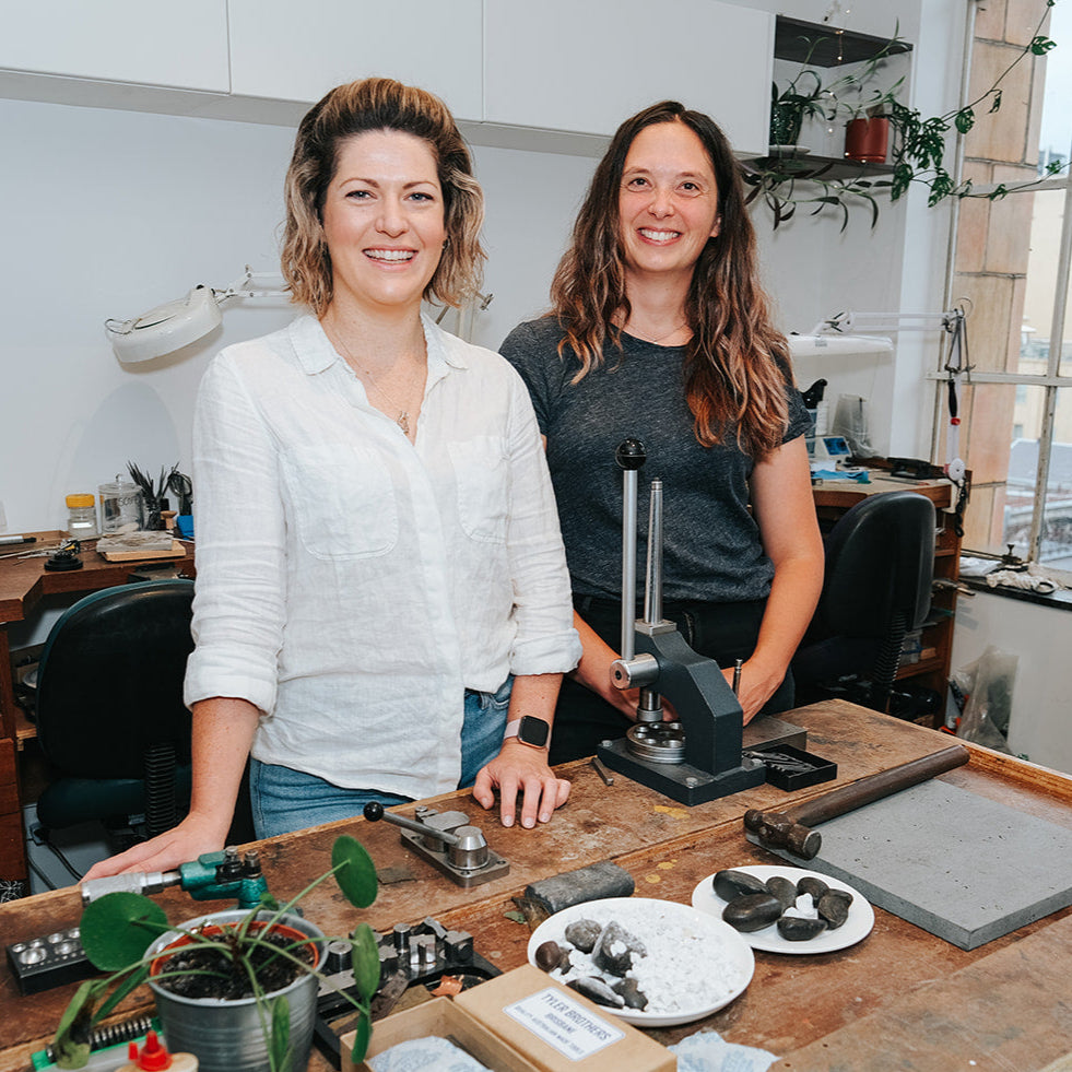 Megan Webb and Jenna Steele stand in their Melbourne studio. They are surrounded by jewellery tools.