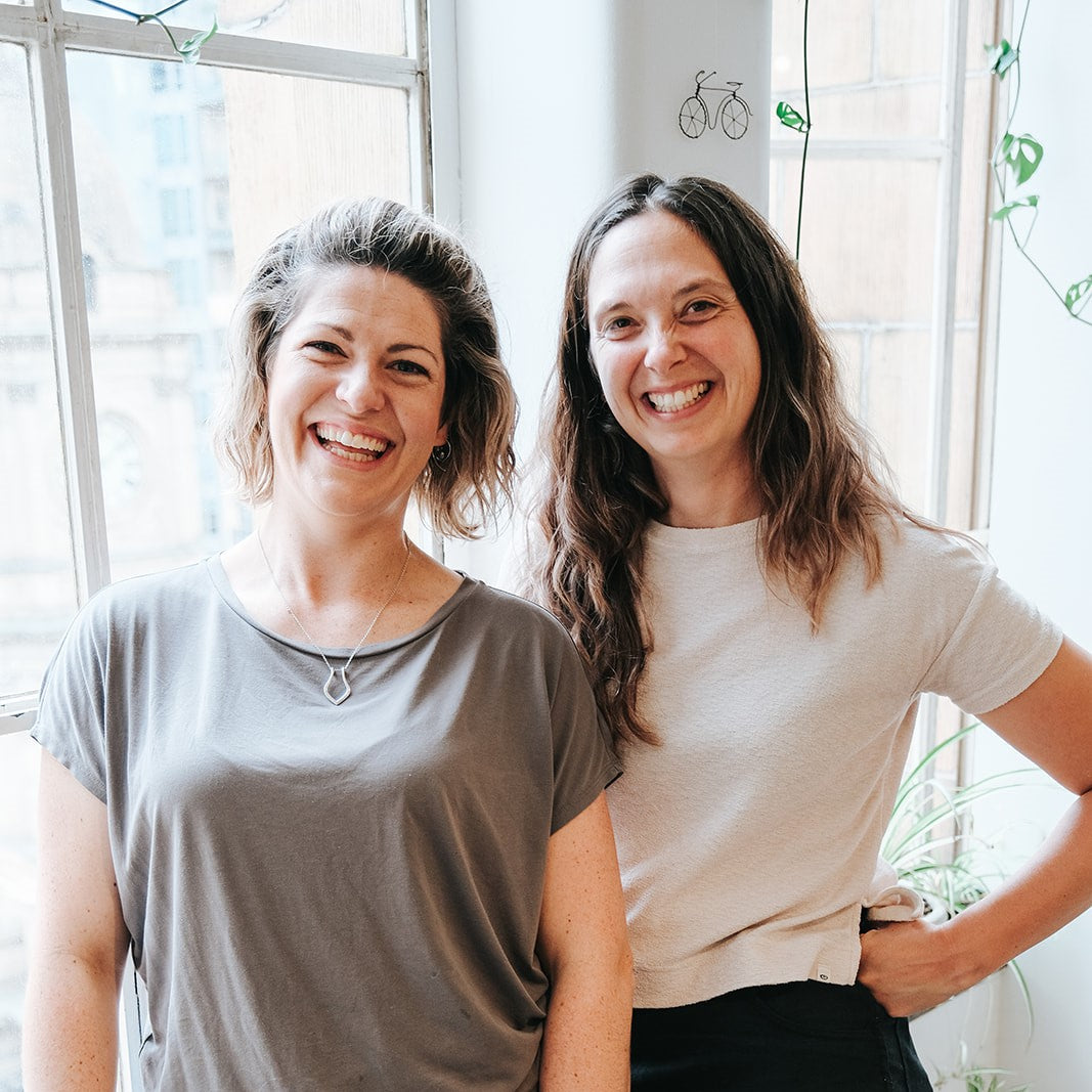 Jenna and Megan standing side by side at the window of their Melbourne studio.