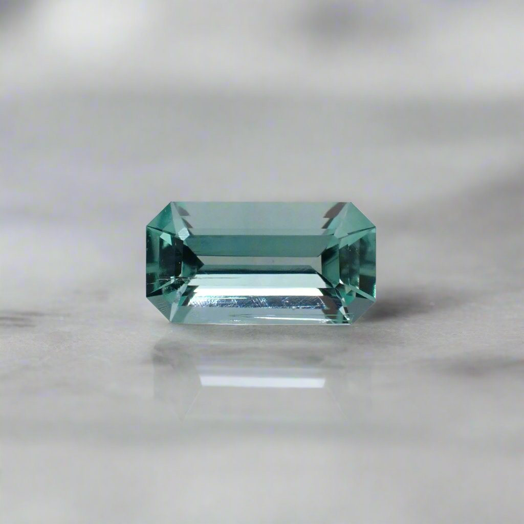 A long emerald in pale green with a blue tint rests on a white surface.