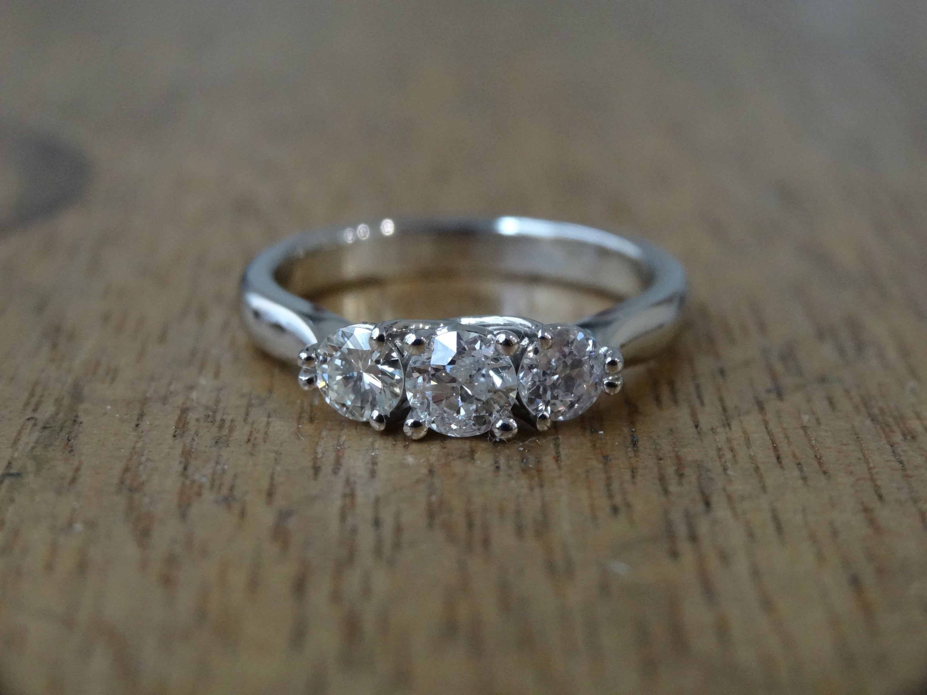 Platinum trilogy engagement ring claw set with three round diamonds on a wooden surface