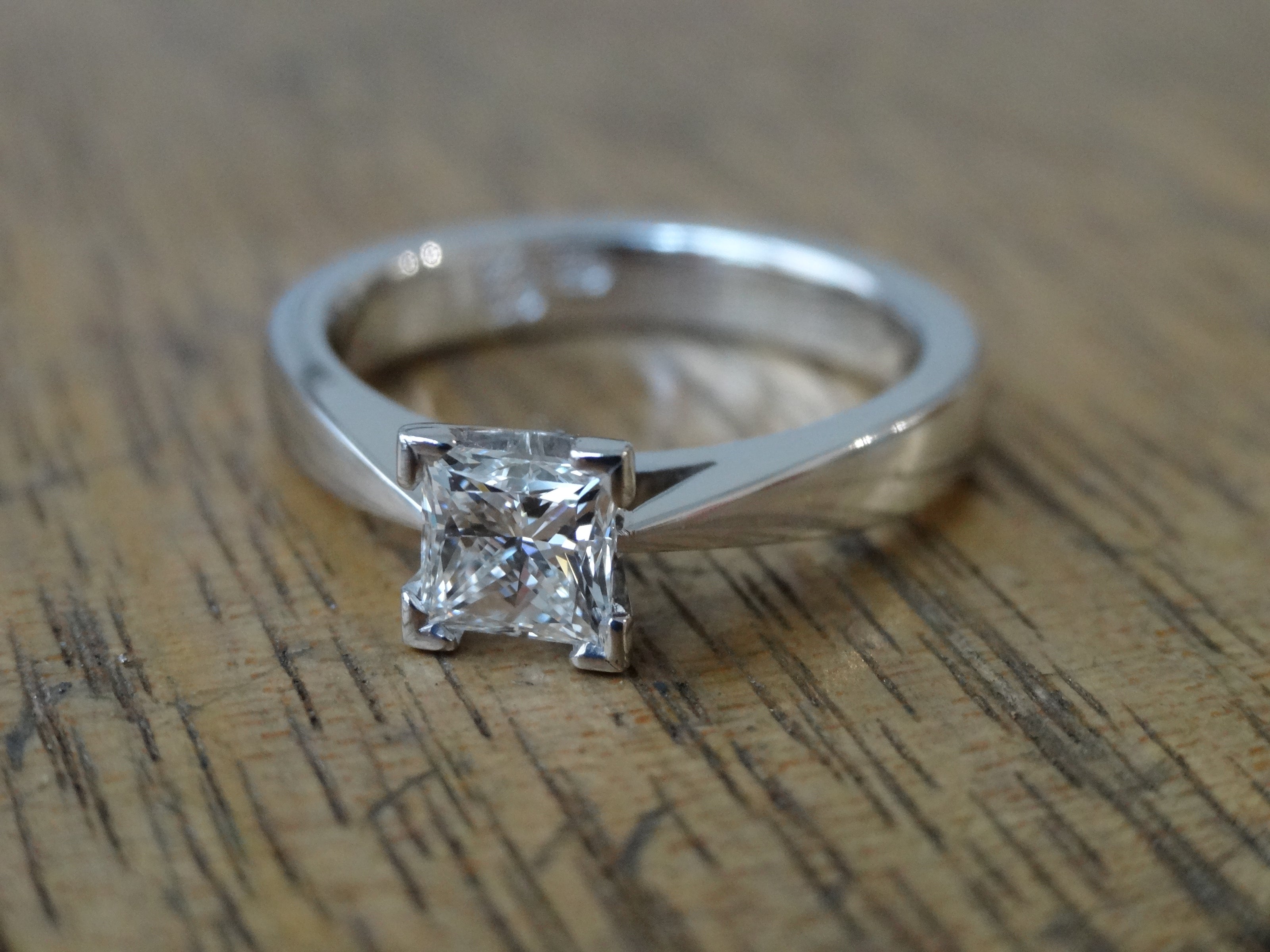 Recycled white gold solitaire engagement ring claw set with one princess cut diamond on a wooden surface