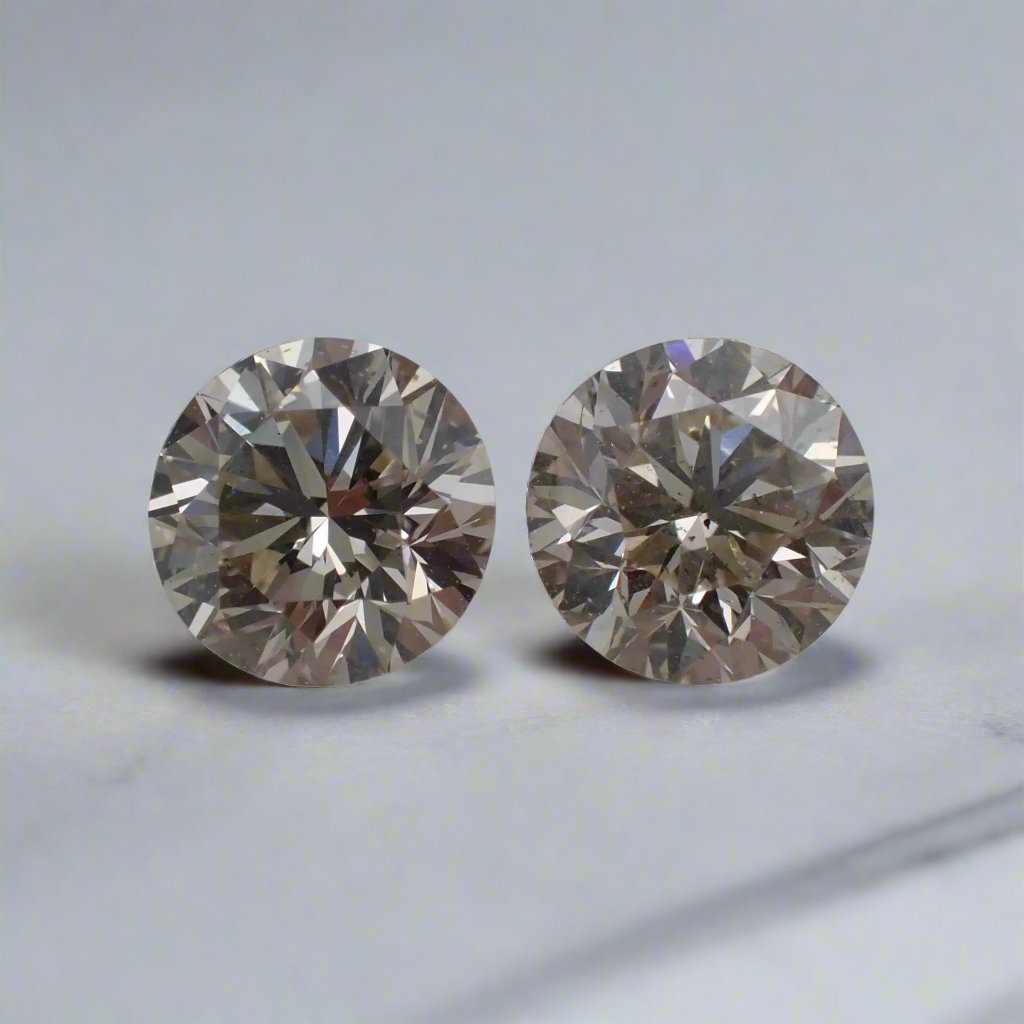 A pair of round, light champagne diamonds rests on a white surface.