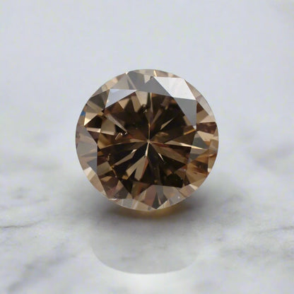 A round brilliant cut, champagne diamond with small bubble inclusions sits loose on a white surface.