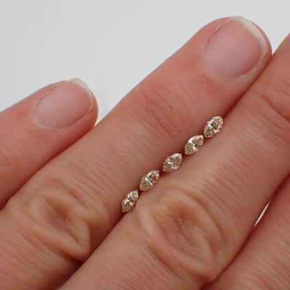 a line of five champagne marquise cut diamonds rests between two fingers